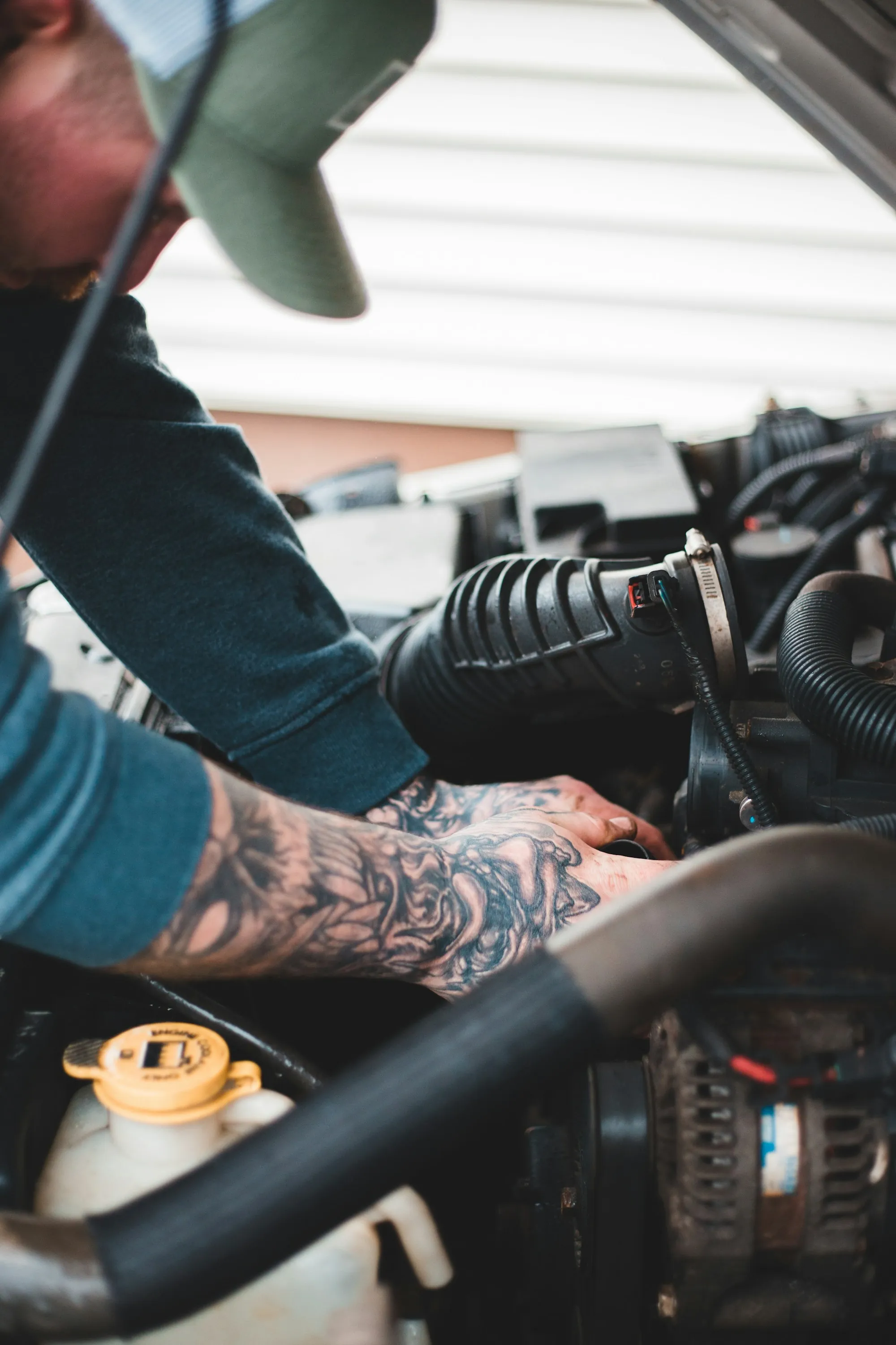 Technician with tattooed forearms tightening a component in an engine bay