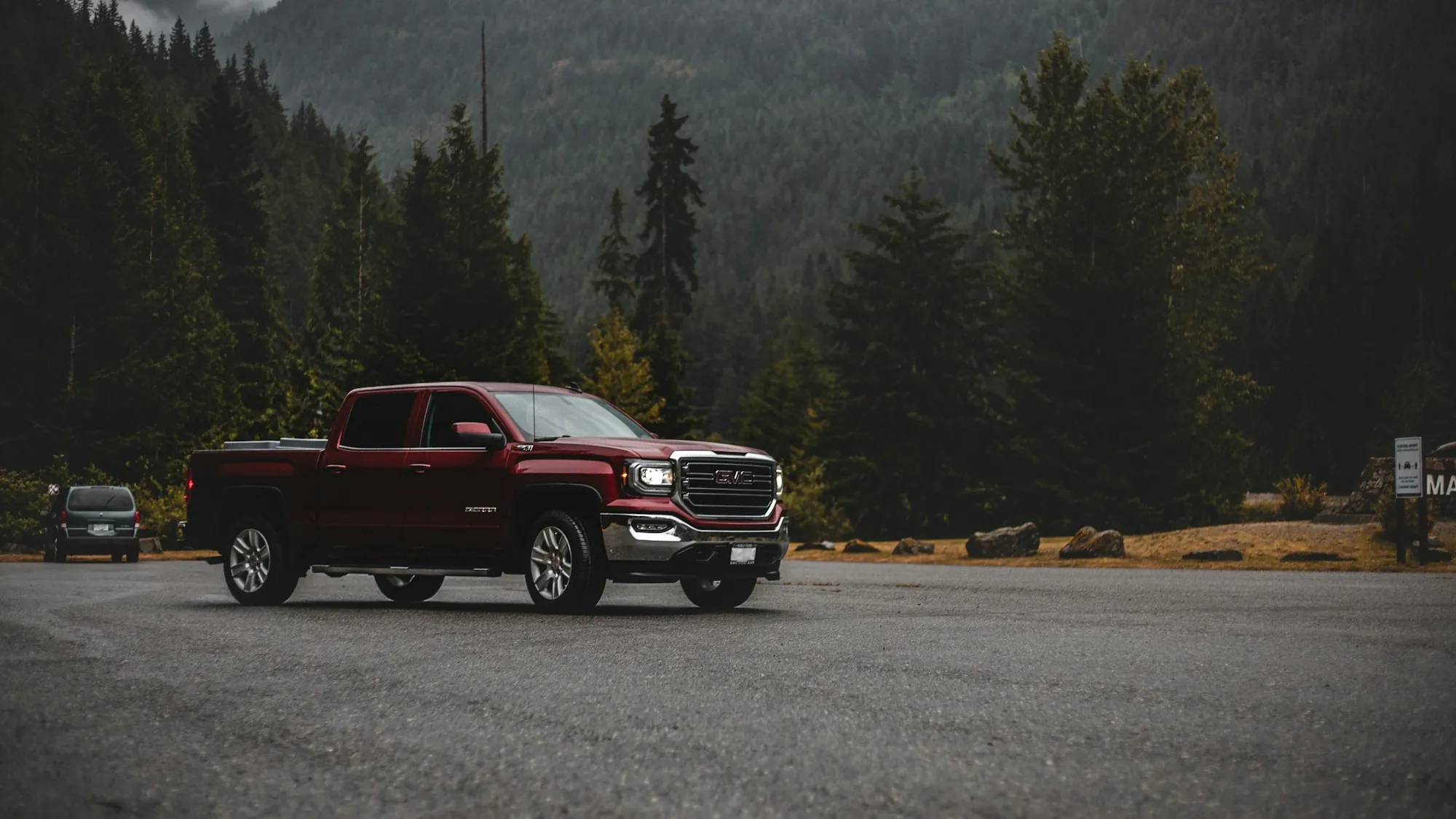 Red pickup truck parked in a forest clearing below the mountains