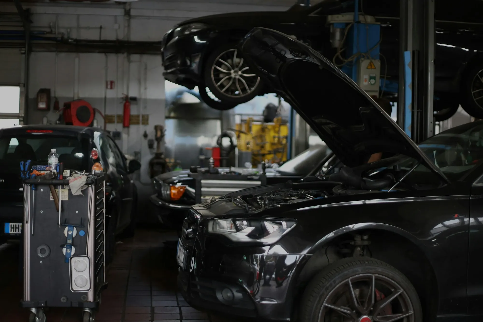 Dark repair bay with a black SUV raised and its hood open