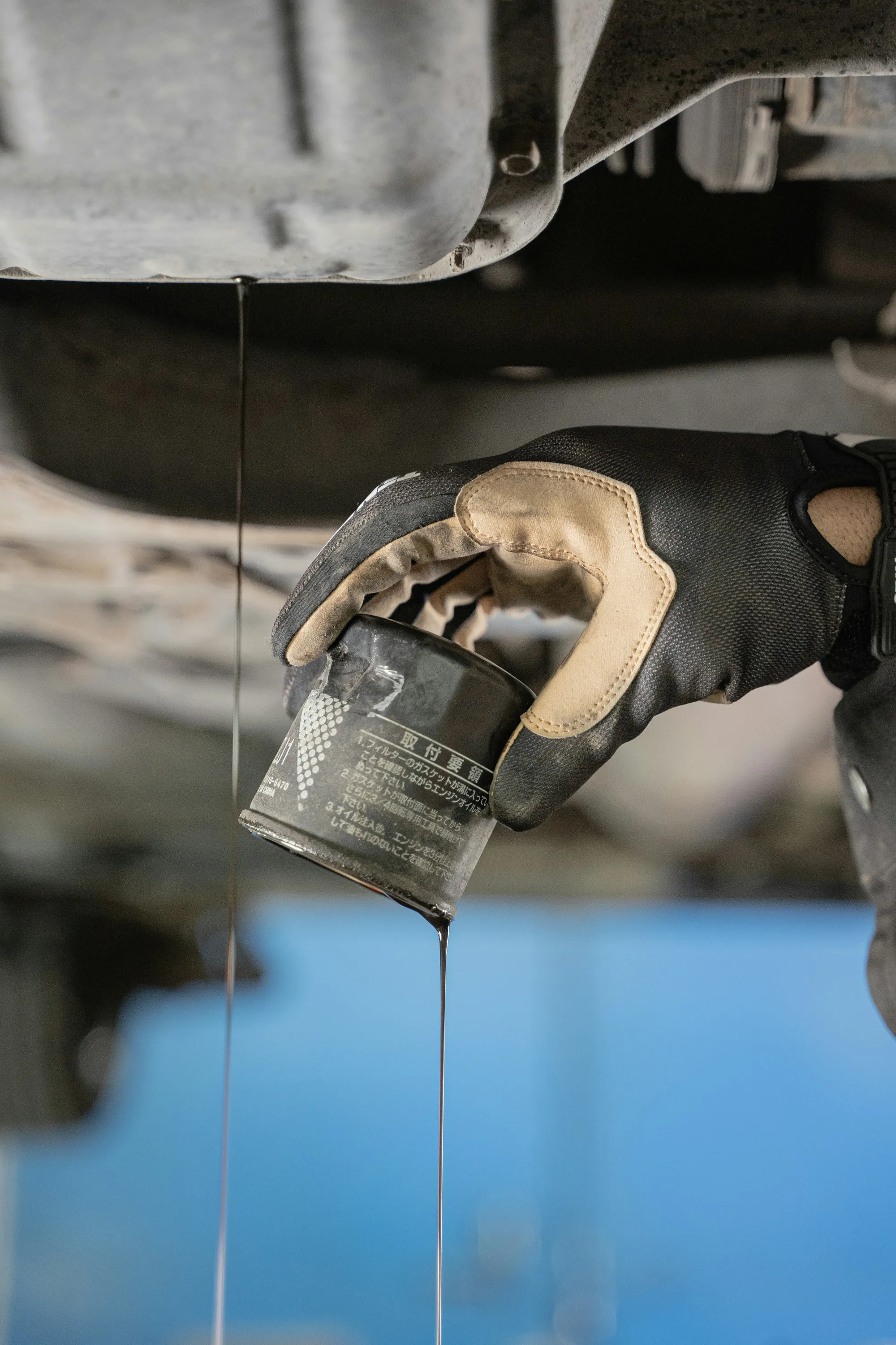 Gloved hand holding a used oil filter beneath a vehicle